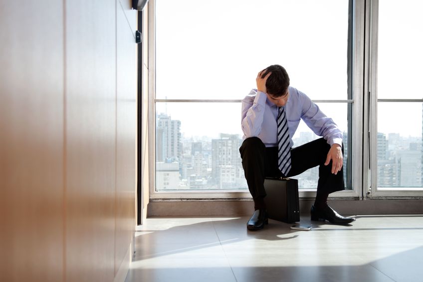 Berufsunfähigkeitsversicherung Burnout - erschöpfter Mann sitzt auf Aktentasche